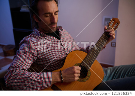 Man playing acoustic guitar while sitting in a cozy room 121856324