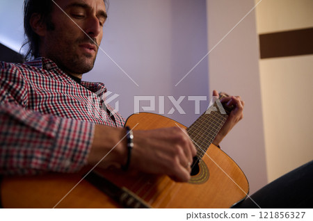 Man playing an acoustic guitar in a relaxed indoor setting Man playing an acoustic guitar in a relaxed indoor setting 121856327