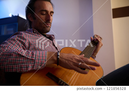 Man strumming an acoustic guitar in a relaxed indoor environment Man strumming an acoustic guitar in a relaxed indoor environment 121856328