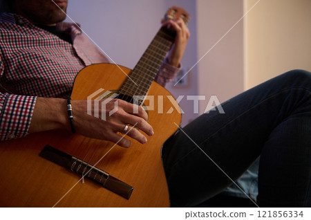 Man relaxing and playing an acoustic guitar indoors wearing casual attire. Man relaxing and playing an acoustic guitar indoors wearing casual attire. 121856334