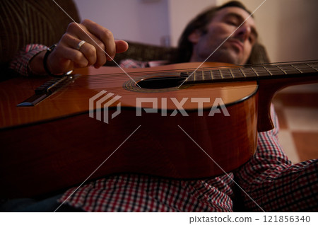 Man relaxing with acoustic guitar lying on a couch in dim light Man relaxing with acoustic guitar lying on a couch in dim light 121856340