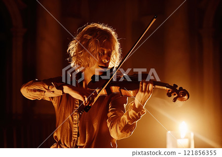 Violinist at a concert playing traditional classical music on a vintage violin. Performer under spotlights in the haze. 121856355