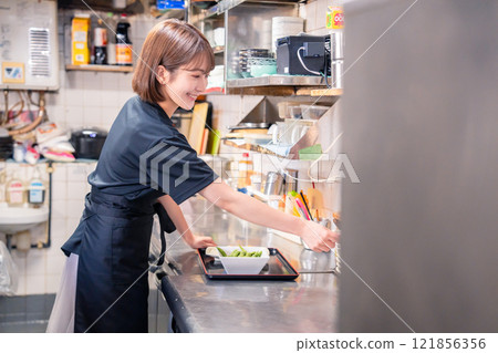 A female kitchen staff member working in the kitchen of an izakaya A female kitchen staff member working in the kitchen of an izakaya 121856356