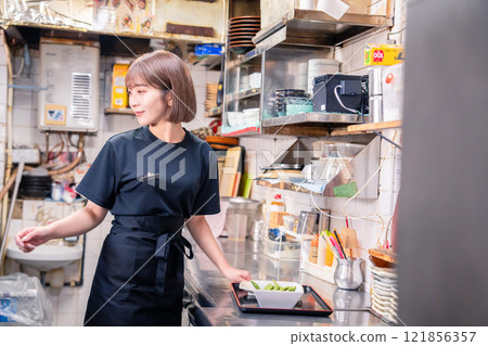 A female kitchen staff member working in the kitchen of an izakaya 121856357