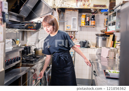 A female kitchen staff member working in the kitchen of an izakaya A female kitchen staff member working in the kitchen of an izakaya 121856362