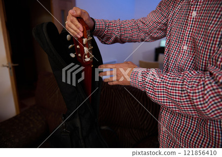 Person packing a guitar into a case inside a cozy indoor setting 121856410