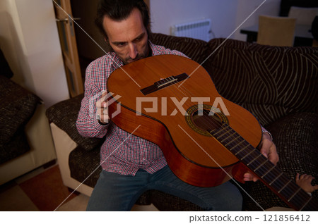 Man inspecting an acoustic guitar in a cozy indoor setting 121856412