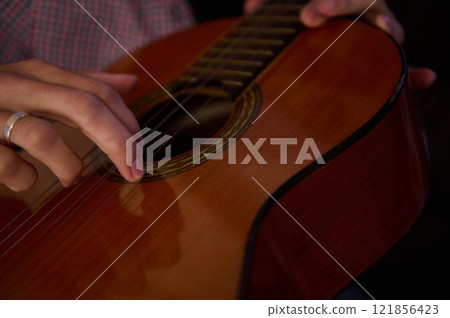 Man playing a classical guitar with focused attention and precision Man playing a classical guitar with focused attention and precision 121856423