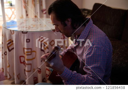 Man playing acoustic guitar in a cozy living room setting 121856438