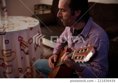 Man playing acoustic guitar in relaxed home setting during leisure time 121856439
