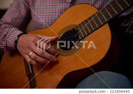 Close-up of a person playing an acoustic guitar indoors Close-up of a person playing an acoustic guitar indoors 121856445