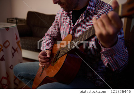Man playing an acoustic guitar in a relaxed indoor setting 121856446