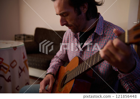 Man playing guitar in a cozy living room setting during leisure time Man playing guitar in a cozy living room setting during leisure time 121856448