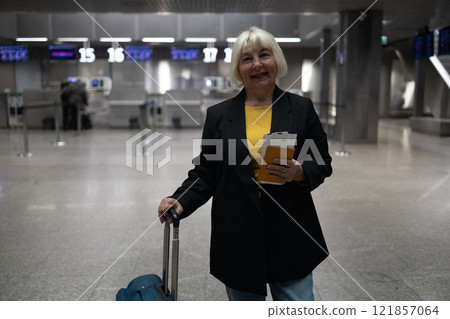 Smiling senior woman in airport looking camera schedule to check flight departure gate. Travel and tourism concept, people with backpack on shoulders. 121857064