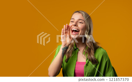 Attention, portrait of young woman shouting, holding hand near open mouth 121857370