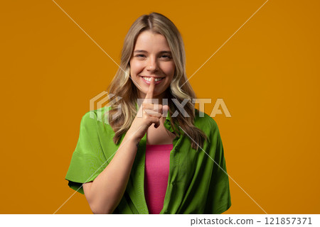 Beautiful stylish woman holding finger on lips, yellow studio background. Pretty lady with gesture of shhh, secret, silence, conspiracy, gossip, rumors concept. Beautiful stylish woman holding finger on lips, yellow studio background. Pretty lady with gesture of shhh, secret, silence, conspiracy, gossip, rumors concept. 121857371
