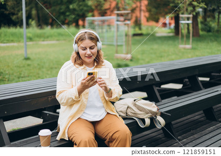 Closeup portrait of a lovely young female listening to music through wireless earphones on nature background. Music lover enjoying music. Woman record voice by mobile cell phone Dictaphone 121859151