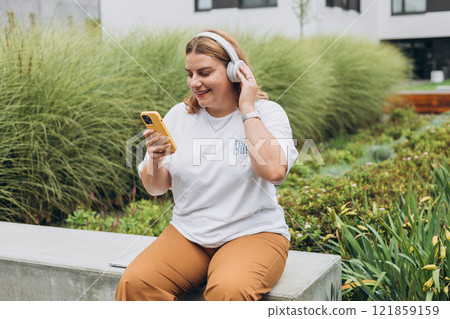 Closeup portrait of a lovely young female listening to music through wireless earphones on urban background. Music lover enjoying music. Woman record voice by mobile cell phone Dictaphone Closeup portrait of a lovely young female listening to music through wireless earphones on urban background. Music lover enjoying music. Woman record voice by mobile cell phone Dictaphone 121859159