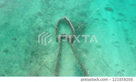 Aerial view of traditional fish trap partially submerged in turquoise waters of Tikehau, a coral atoll reef in pacific ocean tuamotu archipelago. Old style fishing. Aerial drone panorama zoom out 121859208