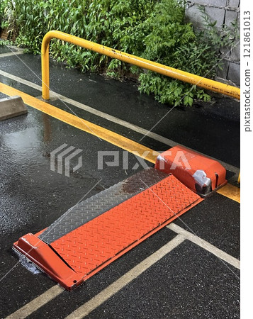 Wet parking lot barrier with reflective orange ramp. Concept of traffic management, urban infrastructure, and safety measures. 121861013