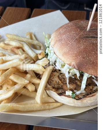 Pulled pork burger with crispy fries on a wooden table, close up. Concept of comfort food, casual dining, eating out and satisfying meals. 121861014