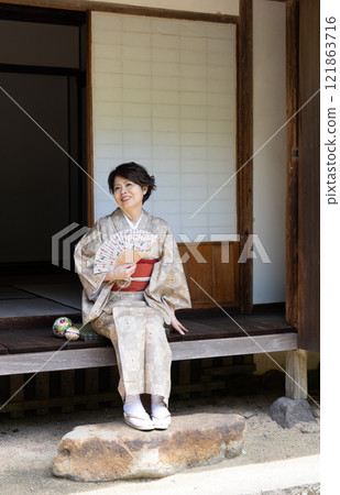 一個穿著和服的女人坐在門廊上用風扇為自己降溫 一個穿著和服的女人坐在門廊上用風扇為自己降溫 121863716