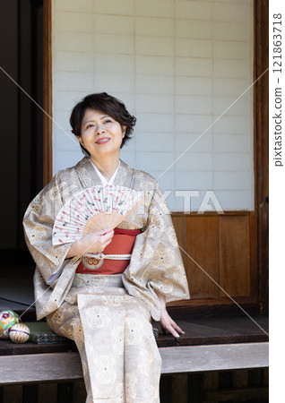 一個穿著和服的女人坐在門廊上用風扇為自己降溫 一個穿著和服的女人坐在門廊上用風扇為自己降溫 121863718