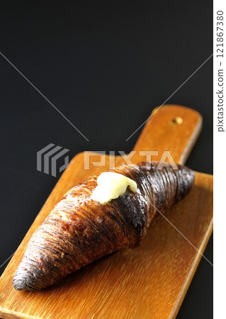 A slightly burnt black wasan on a cutting board photographed against a black background 121867380