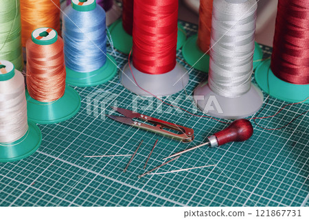 Multi-colored bobbins with threads for stitching leather and tanners tools on a cutting mat, selected focus. 121867731