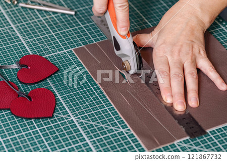 Tanners hands cut leather using work tool on a green cutting mat, close-up, process. Tanners hands cut leather using work tool on a green cutting mat, close-up, process. 121867732