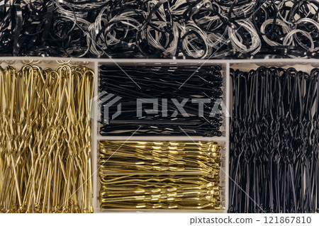Black and golden hairpins of different sizes and hair scrunchie on plastic box, flat lay, close-up. 121867810