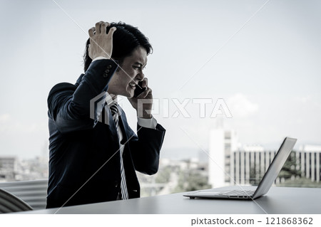 一位年輕的亞洲商人在辦公室使用筆記型電腦打電話(壓力、騷擾、單色、黑白) 一位年輕的亞洲商人在辦公室使用筆記型電腦打電話(壓力、騷擾、單色、黑白) 121868362