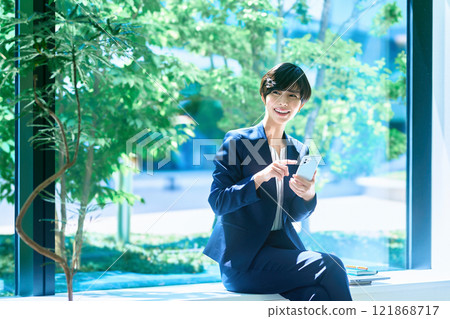 A middle-aged business woman in a suit operating a smartphone in the office Photography cooperation: LINK FOREST A middle-aged business woman in a suit operating a smartphone in the office Photography cooperation: LINK FOREST 121868717