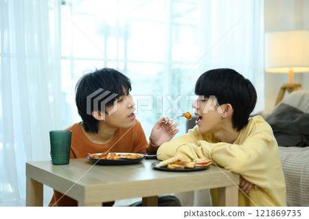 Sweet gay couple enjoys breakfast together in bright living room Sweet gay couple enjoys breakfast together in bright living room 121869735