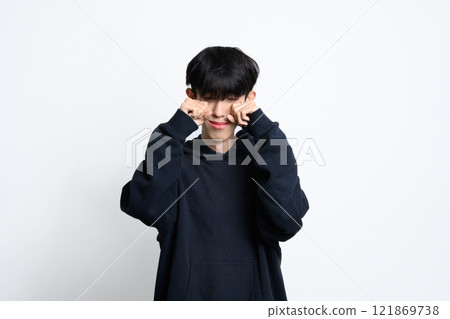 Young man in black hoodie crying and wiping tears over white background Young man in black hoodie crying and wiping tears over white background 121869738