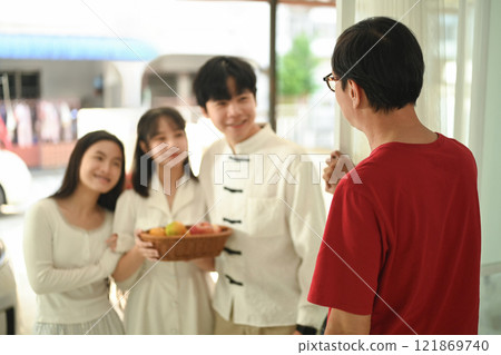 Cheerful family arriving at a relative home during Chinese New Year, carrying a basket of fruits as a gift 121869740