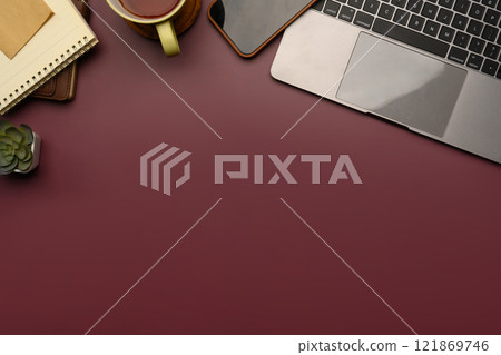Top view of sleek workspace with laptop, smartphone, coffee mug and notebook on burgundy desk 121869746