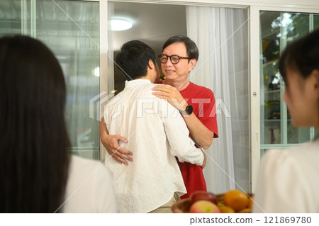 Senior father warmly hugging his son at the entrance of home during Chinese New Year festivities 121869780