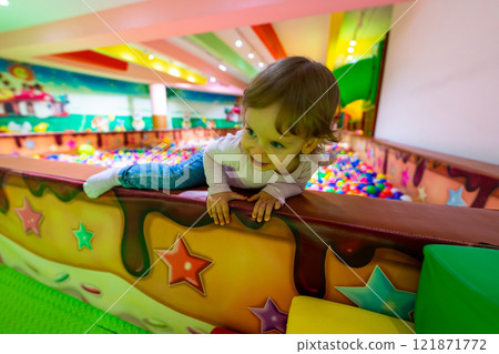 A playful child climbing over a colorful wall in a vibrant indoor playground. 121871772