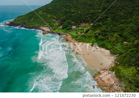 Drone view of a secluded beach with turquoise waters, surrounded by lush forest, rocky coastline, and scattered houses in Brazil. Drone view of a secluded beach with turquoise waters, surrounded by lush forest, rocky coastline, and scattered houses in Brazil. 121872230