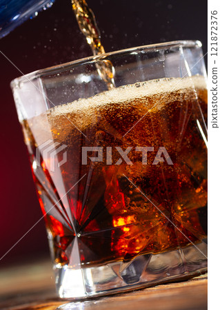 Cola is poured into a glass with ice cubes on a dark background close-up Cola is poured into a glass with ice cubes on a dark background close-up 121872376