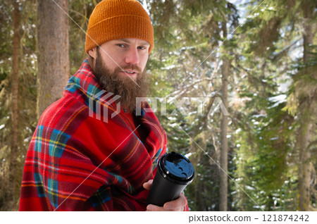 Winter season, snowy landscape adult man walking in the forest on a sunny day, stopped to drink coffee or tea covered with a blanket Winter season, snowy landscape adult man walking in the forest on a sunny day, stopped to drink coffee or tea covered with a blanket 121874242
