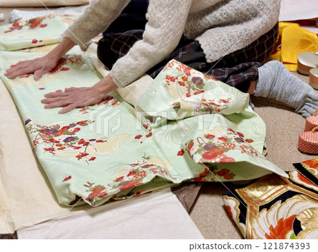 An elderly woman folds a pale green kimono on wrapping paper 121874393