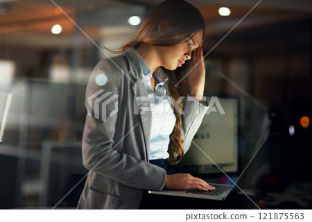 Stressed, worried and tired female entrepreneur typing on a laptop and working overtime late at night. Frustrated and overworked young businesswoman with a headache doing a project with a deadline 121875563