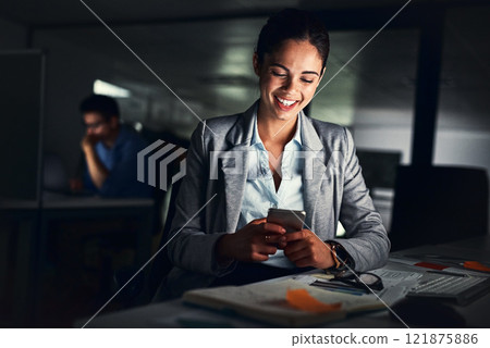 Woman reading text late on phone, smiling at a message and looking at social media posts online while working in a dark office at night. Happy corporate worker checking emails and doing overtime 121875886