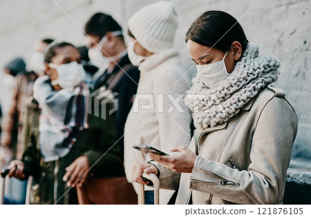 People or tourists traveling during covid and standing in line at a public travel facility wearing protective masks. Woman in a queue reading social media news about coronavirus pandemic on her phone 121876105