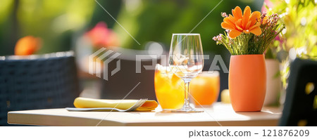 vibrant outdoor dining area featuring creative setup with glass of drink, flower vase, and beautifully arranged table. warm sunlight enhances inviting atmosphere 121876209