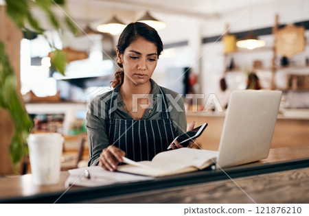 Cafe owner with laptop, phone and book checking online order, searching available bookings and preparing takeaway deliveries coffee shop. Serious local restaurant entrepreneur pricing a menu on tech Cafe owner with laptop, phone and book checking online order, searching available bookings and preparing takeaway deliveries coffee shop. Serious local restaurant entrepreneur pricing a menu on tech 121876210