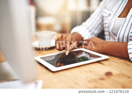 Female african hand using a tablet at a desk doing office work. Closeup of a professional woman browsing on social media while having a cup of tea or coffee. Businesswoman doing research online. 121876228