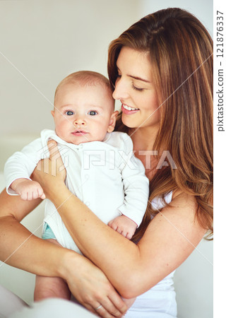 Beautiful family portrait of mother and baby boy hugging, bonding at home, carefree and loving. Smiling, cheerful parent embracing her newborn, enjoying the bond of parenthood and excited to be a mom 121876337